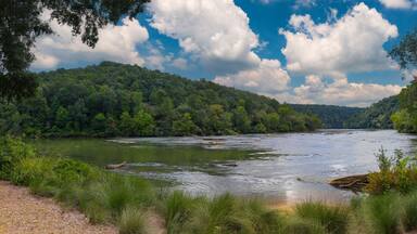 a panoramic of a gorgeous summer landscape on the Chattahoochee River with flowing water surrounded by lush green trees, grass and plants and blue sky with clouds at Walton On The Chattahoochee