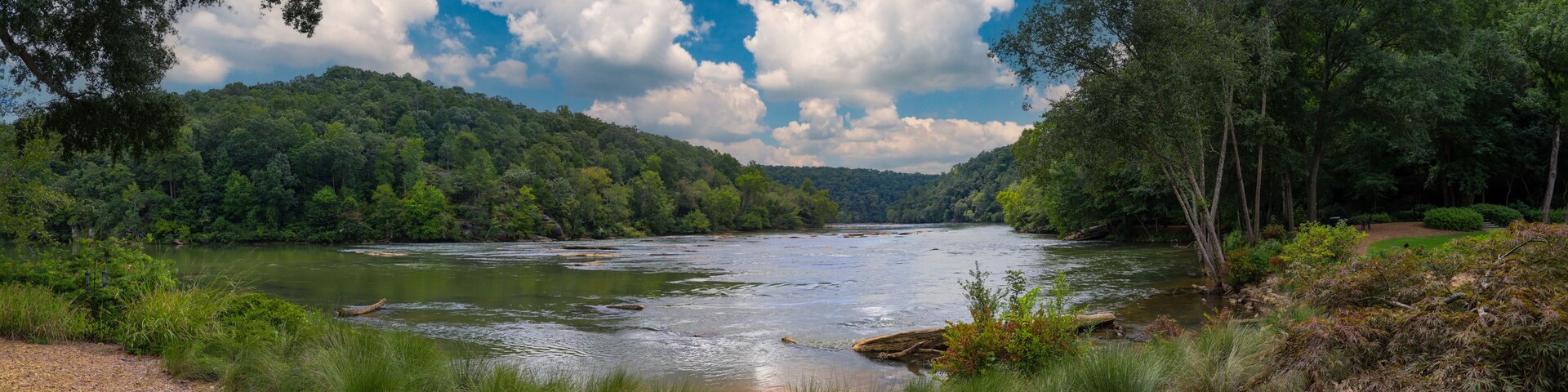 A river flowing through a forested valley with a clear sky above.
