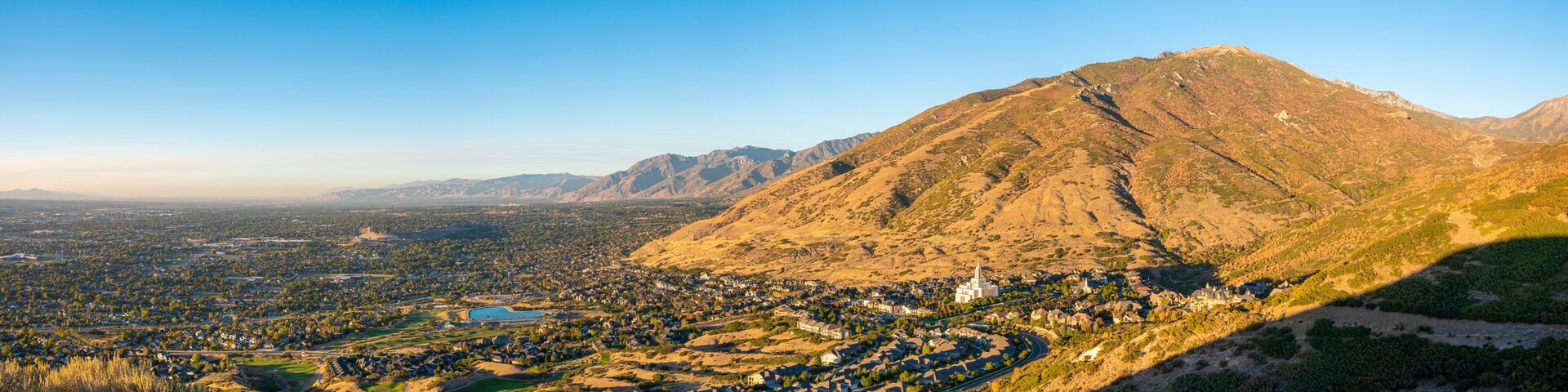 Una montaña con un pueblo a su pie, un cielo azul despejado y una gran masa de agua en la distancia.