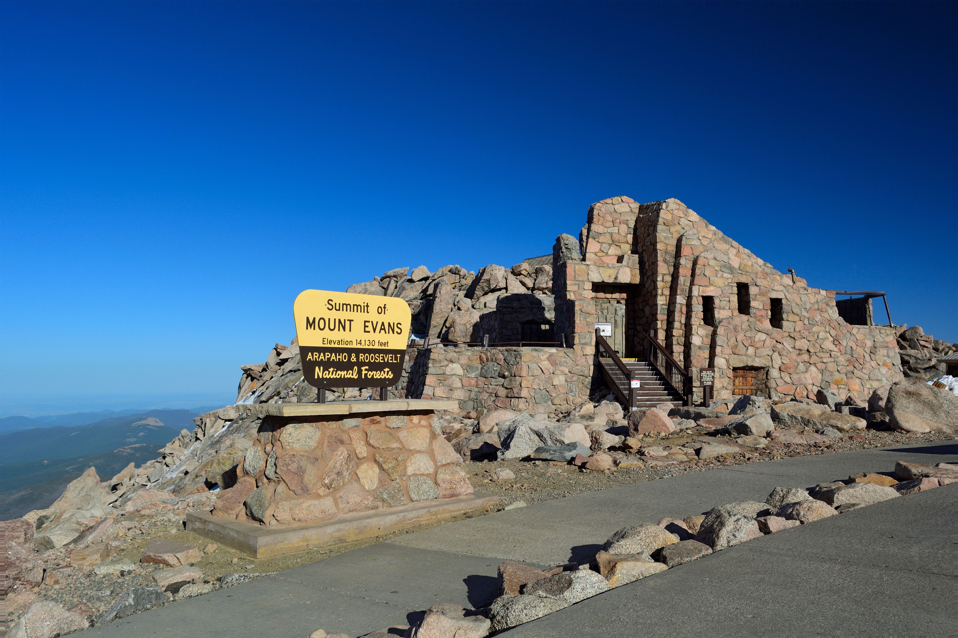 A stone building with a sign reading "Summit of Mount Evans, 14,130 feet, Arapahoe & Roosevelt National Forests."