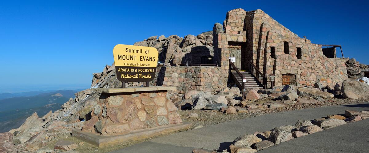 A stone building with a sign reading "Summit of Mount Evans, 14,130 feet, Arapahoe & Roosevelt National Forests."