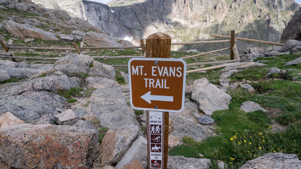 A sign for Mt. Evans Trail with a rocky landscape and mountains in the background.