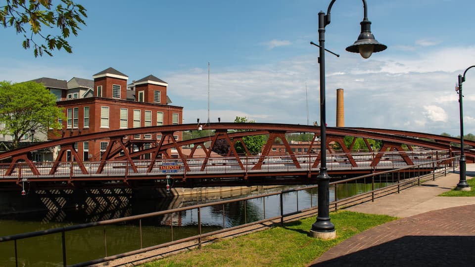 A red metal bridge over a canal with a brick building in the background.