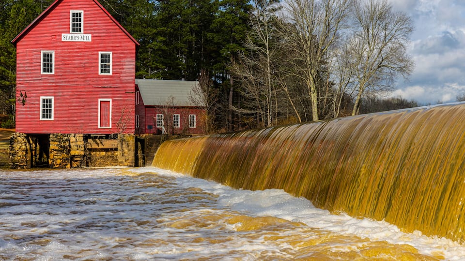 A red mill building with a waterfall in front.