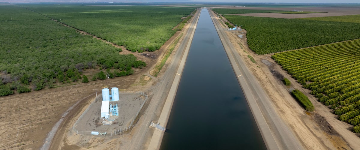 A large waterway flanked by agricultural fields and a distant mountain range.