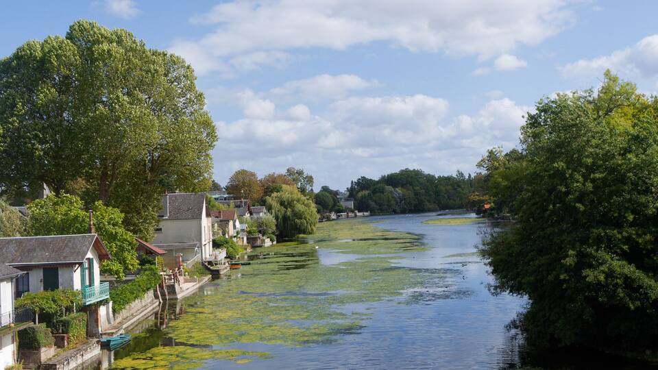A calm river with houses on one bank and trees on the other.