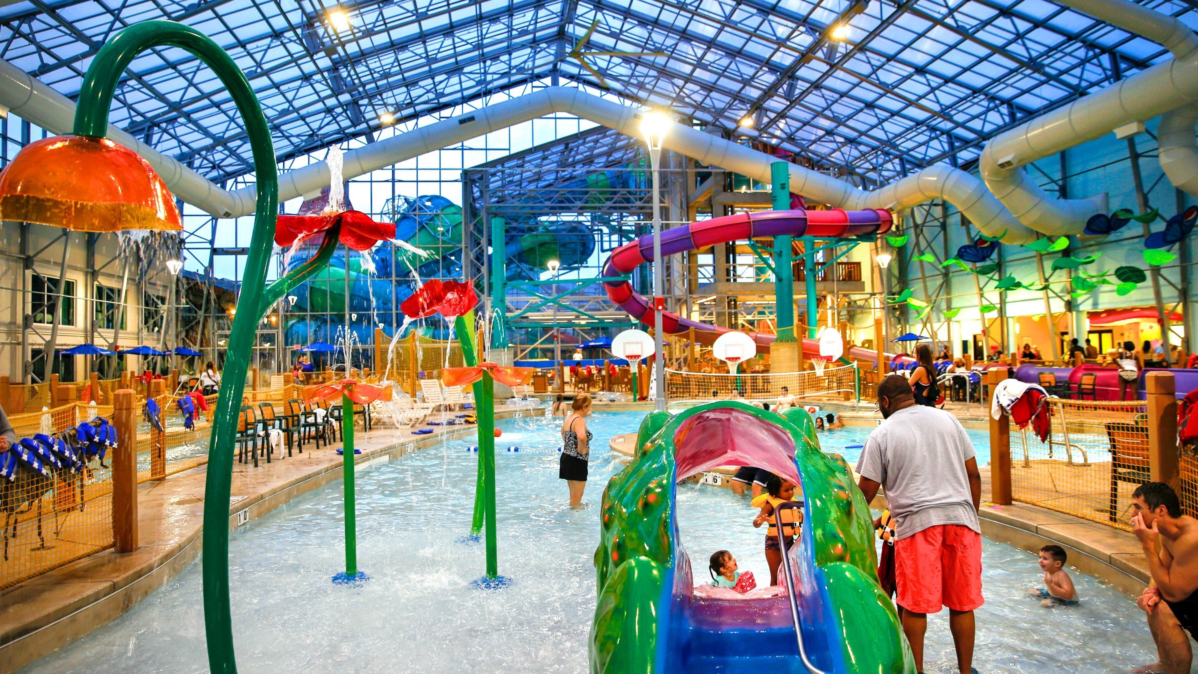 An indoor water park with slides, pools, and a large glass ceiling.