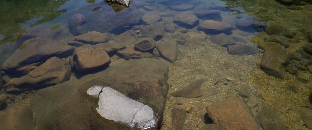 A clear stream with large rocks and pebbles.