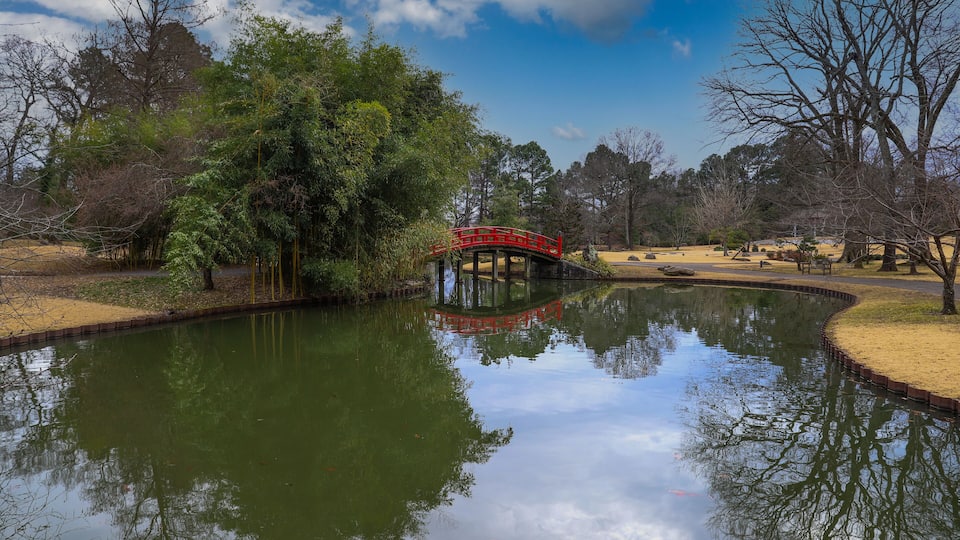 A red bridge over a pond with trees and a clear sky.