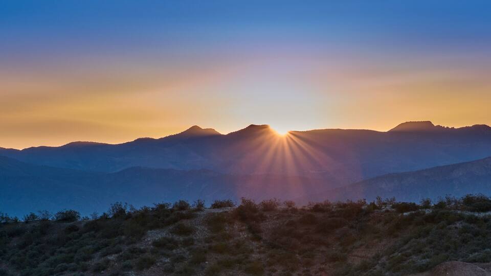 A mountain range with the sun setting behind the peaks.