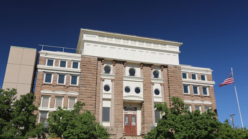 A historic building with a prominent American flag, large windows, and a central entrance with a red door.