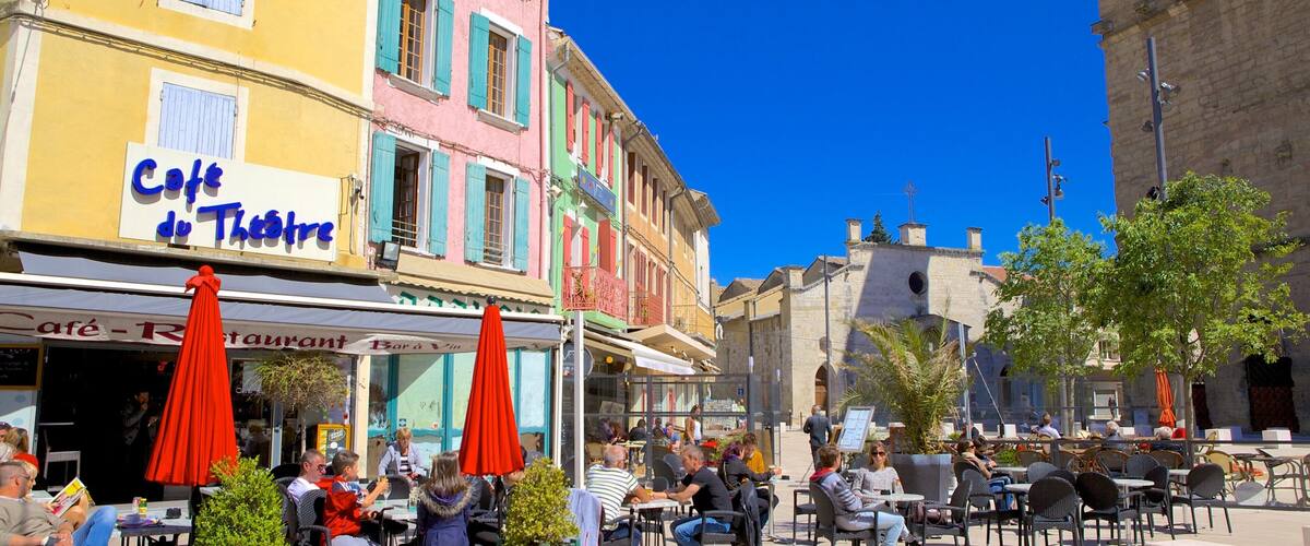 A bustling outdoor café with colorful buildings and patrons enjoying the sunny weather.
