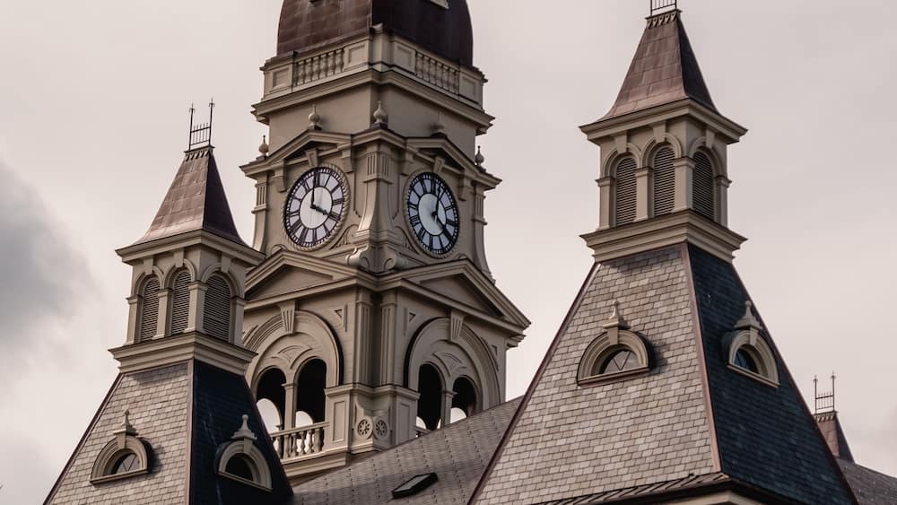 A historic building with a prominent clock tower, arched windows, and a weather vane.