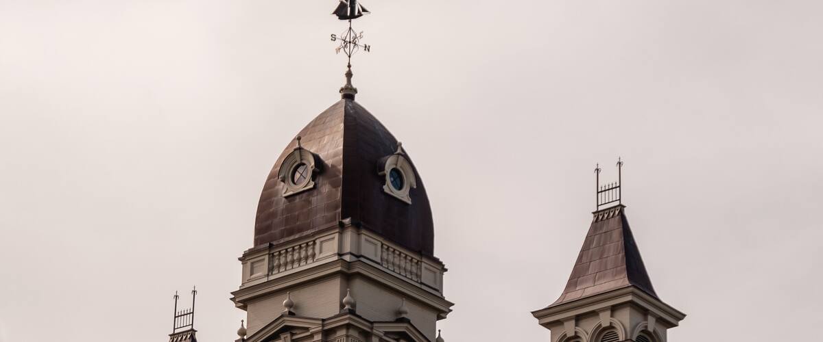 A historic building with a prominent clock tower, arched windows, and a weather vane.