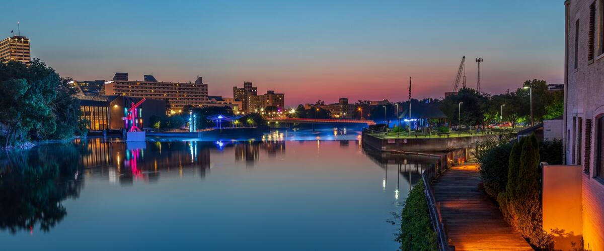 A calm river at dusk with illuminated structures and a bridge.