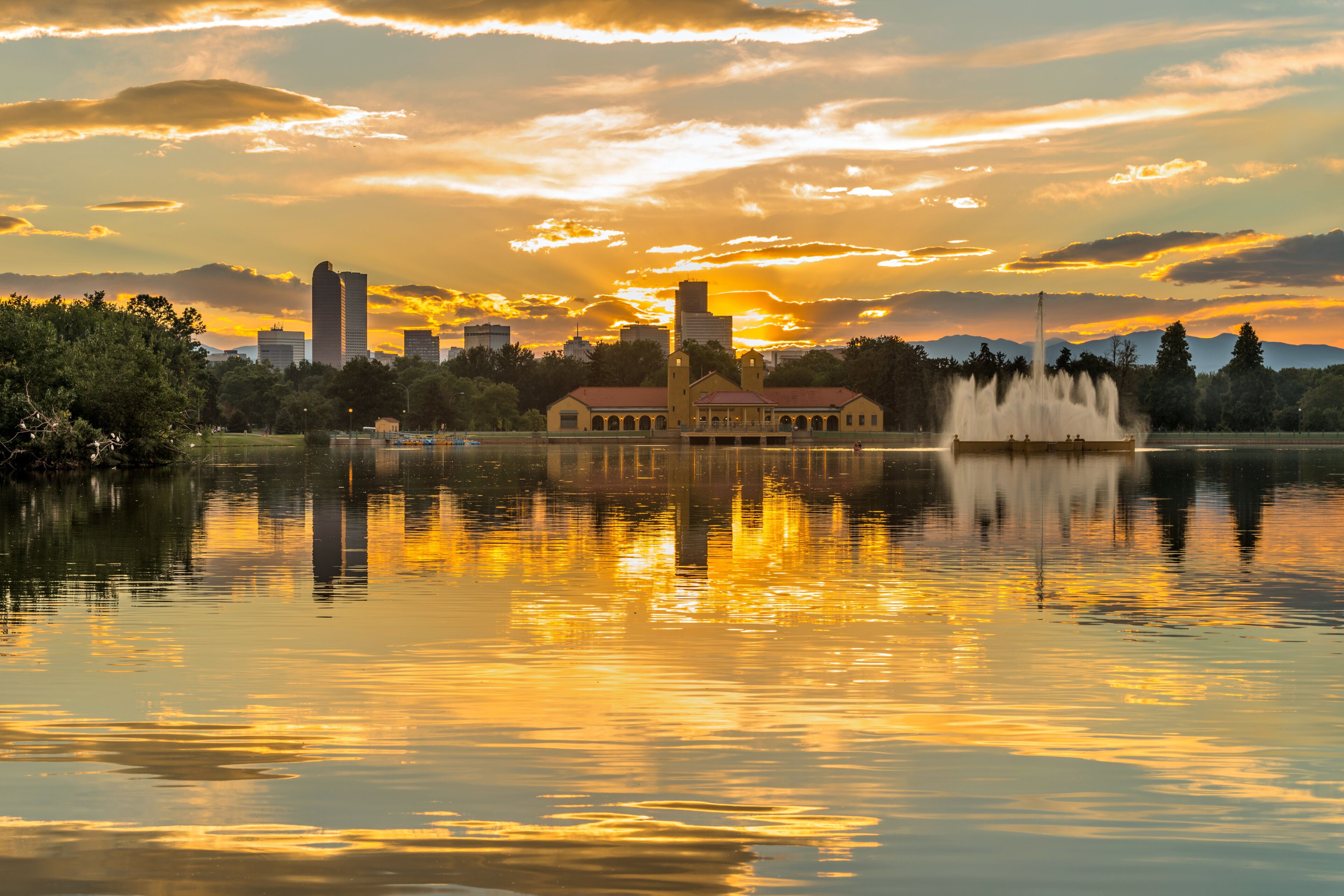 Um pôr do sol sobre um lago, com o horizonte da cidade ao fundo.