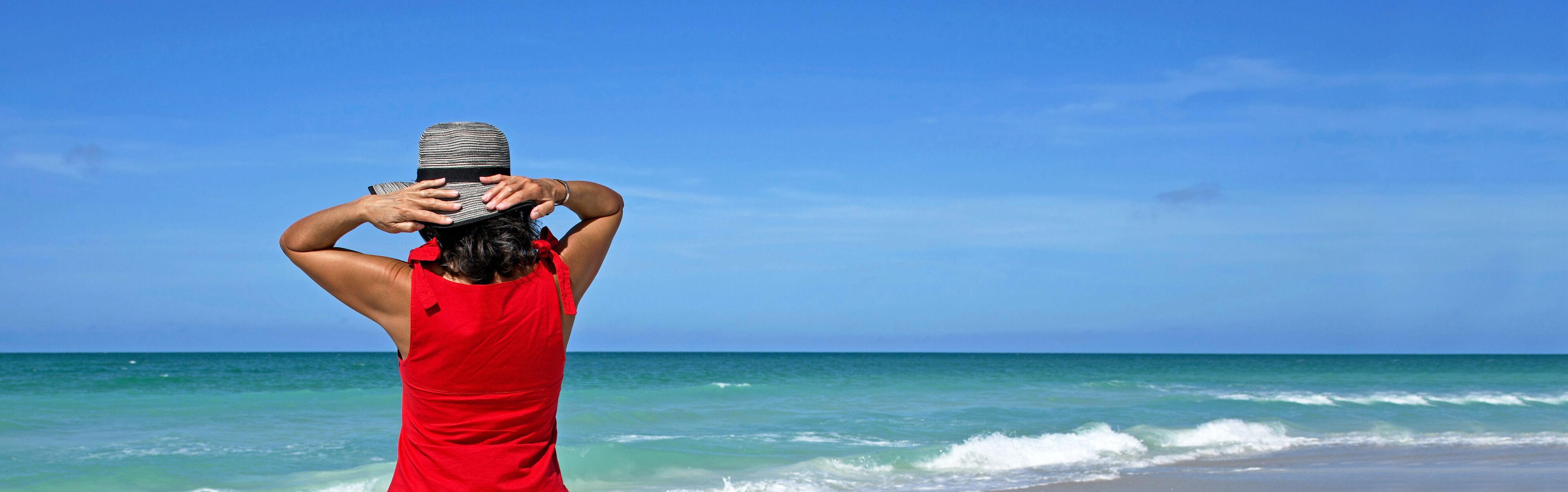 A person in a red dress standing at the beach with waves in the background.