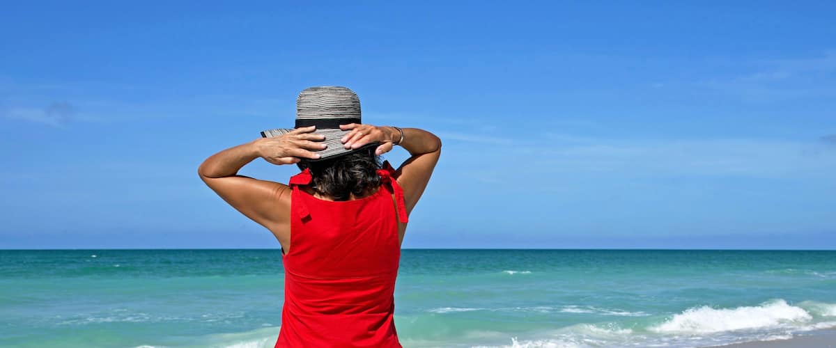 A person in a red dress standing at the beach with waves in the background.