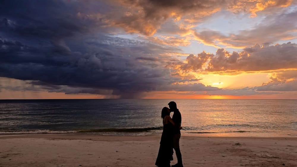 Ein Paar umarmt sich am Strand bei Sonnenuntergang, der Himmel präsentiert ein dramatisches Schauspiel.