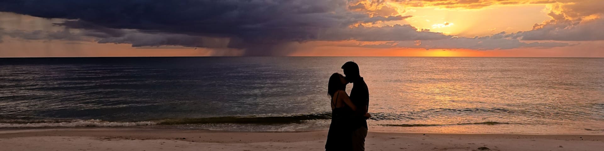 A couple embracing on a beach at sunset with a dramatic sky.