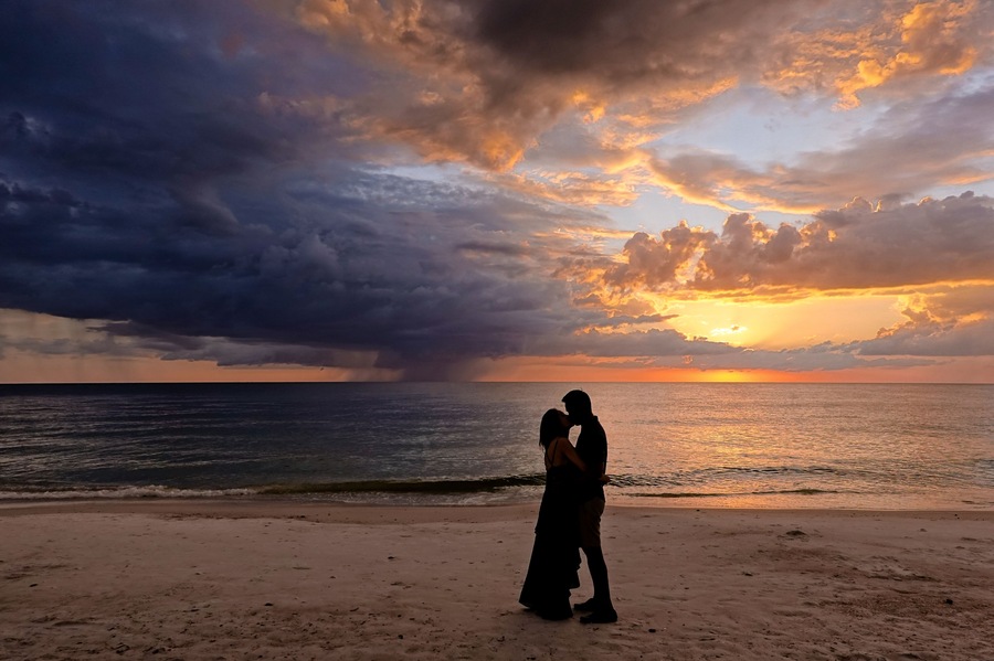 Ein Paar umarmt sich am Strand bei Sonnenuntergang, der Himmel präsentiert ein dramatisches Schauspiel.