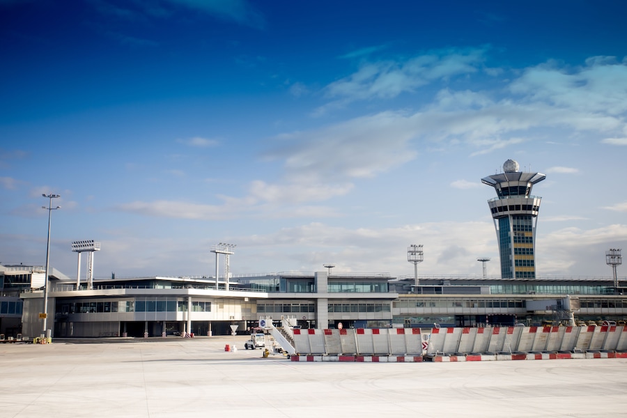 Una terminal de aeropuerto con una torre de control, cielo despejado y una plataforma con barreras.