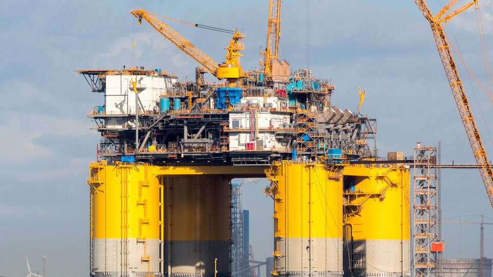 A large industrial structure with yellow and gray sections, surrounded by water, and a crane in the background.