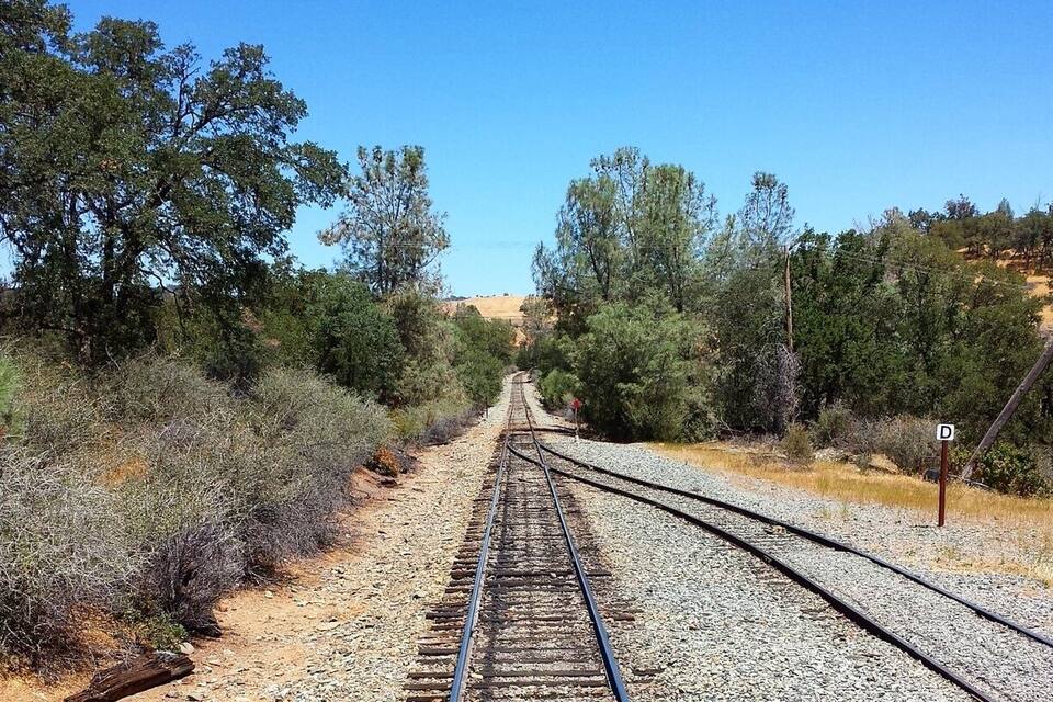 A railway track extending into the distance, surrounded by dry vegetation and trees.