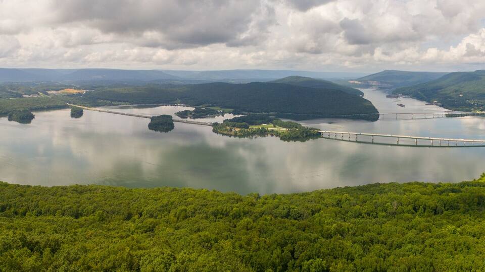 A large lake surrounded by dense forest and hills, with a bridge crossing the water.