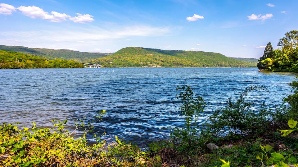 A lake with a bridge, surrounded by green hills and clear blue sky.