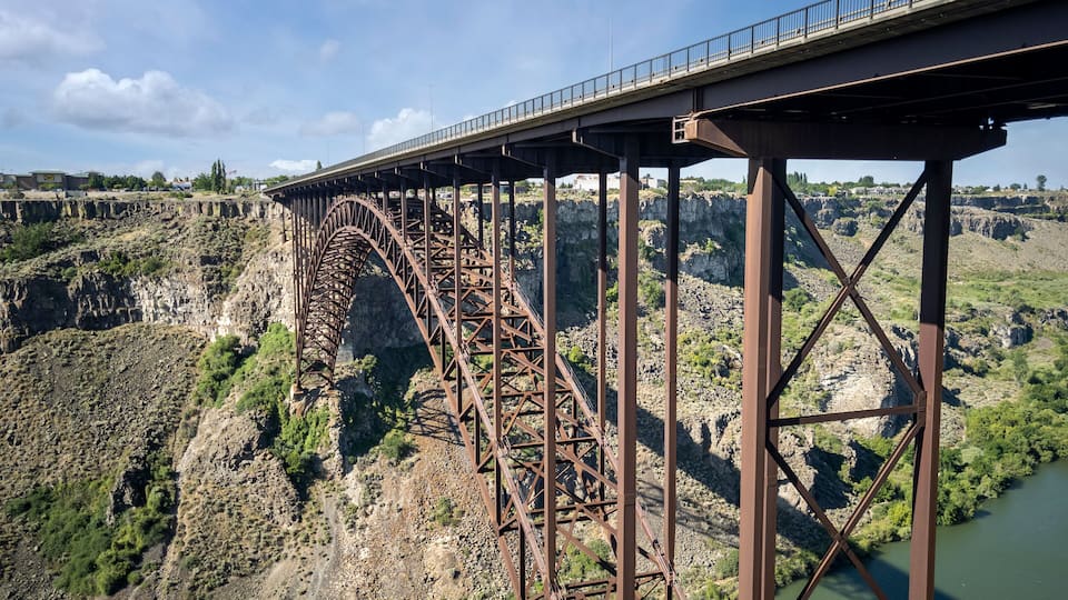 A steel bridge spanning a deep gorge with rocky terrain and sparse vegetation.
