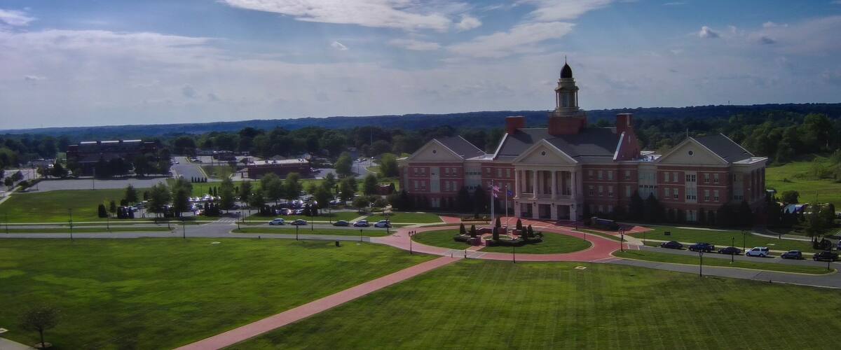 A large red brick building with a tower, surrounded by green lawns and a parking lot.