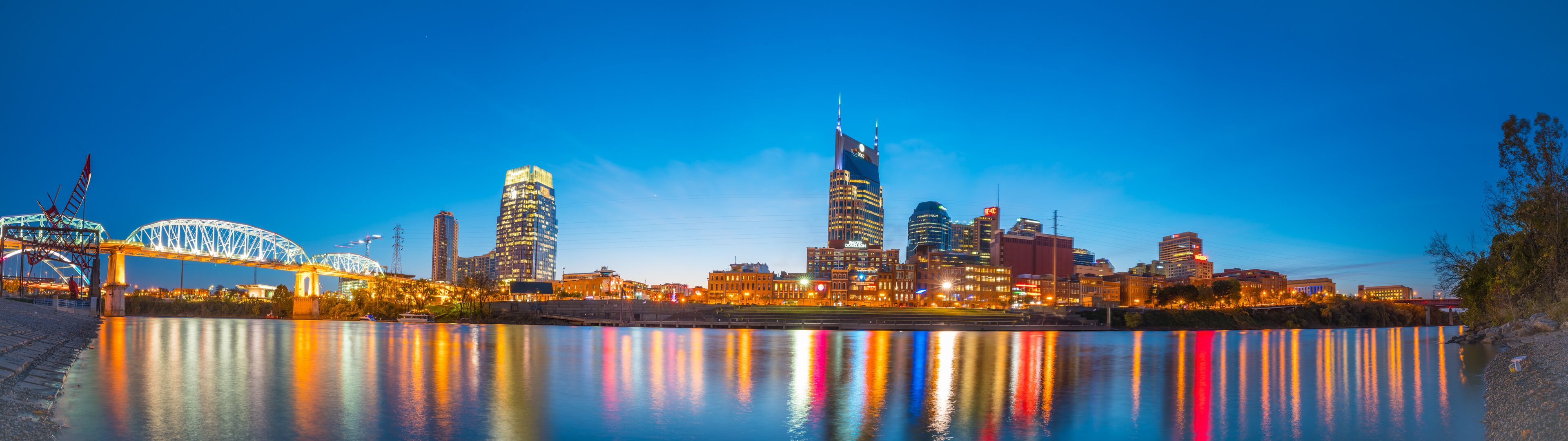 A city skyline at dusk with illuminated buildings reflecting on the water.