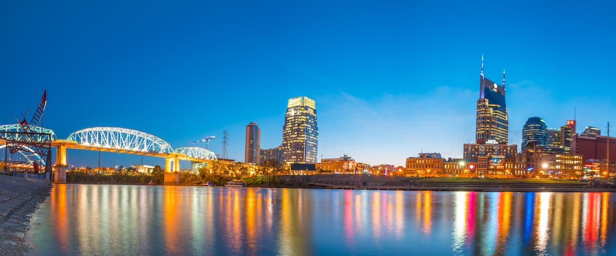 A city skyline at dusk with illuminated buildings reflecting on the water.