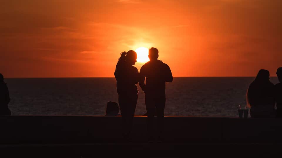 A sunset over the ocean with silhouettes of people on a pier.