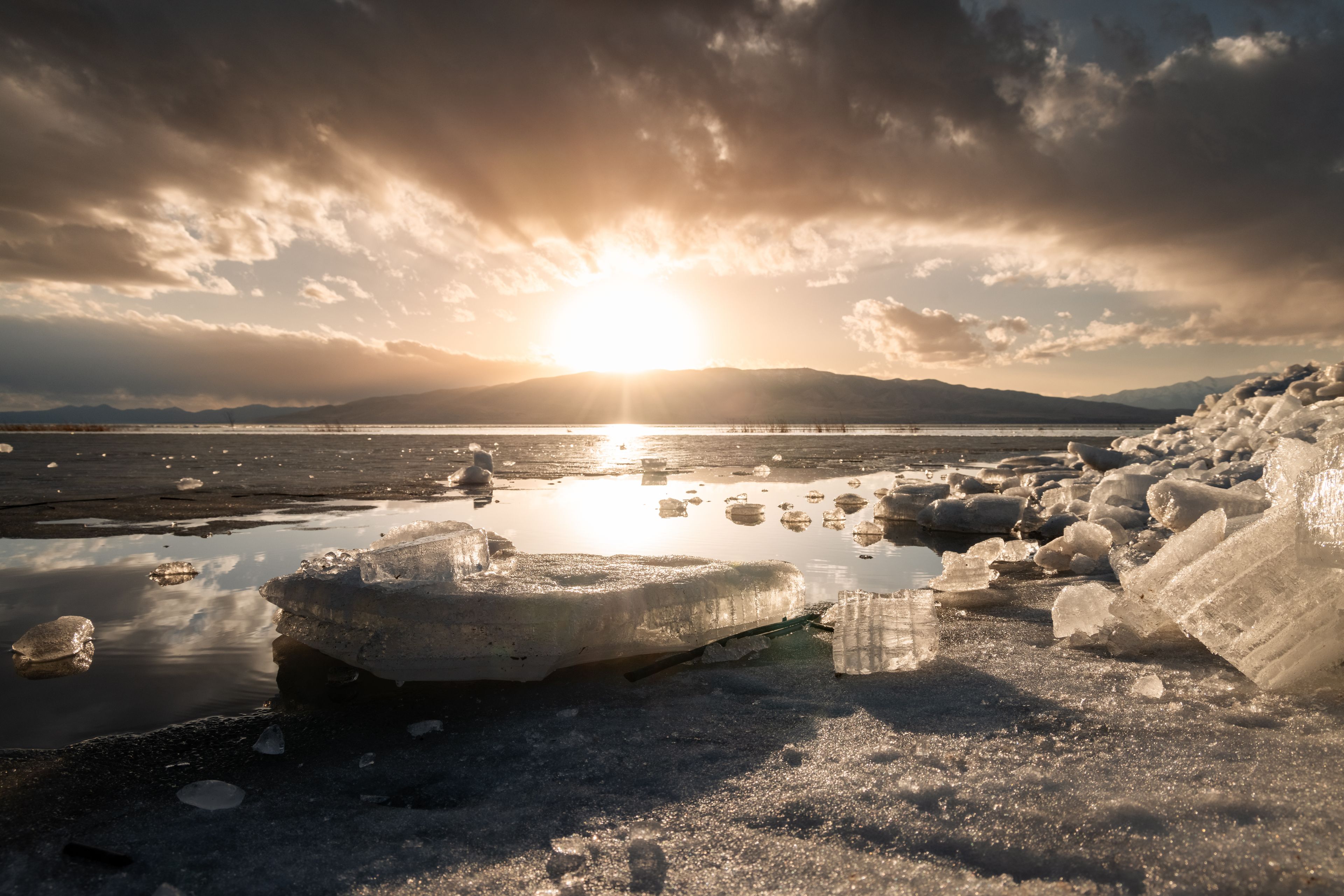 A frozen lake with icebergs and a sunset in the background.