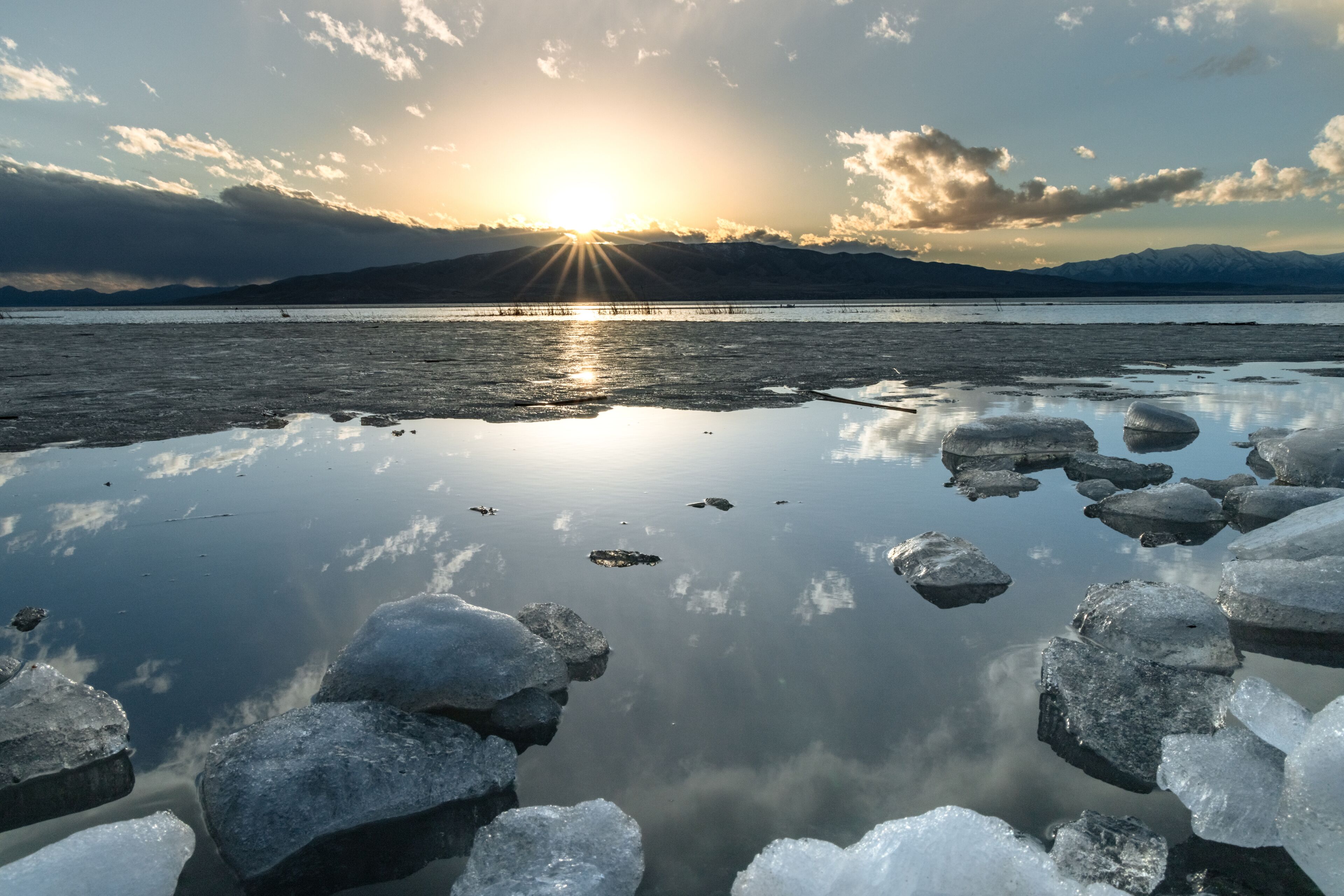 Ice stacks in horizontal image at Vineyard Beach on Utah Lake in Utah at sunset with sun star in February 2025.