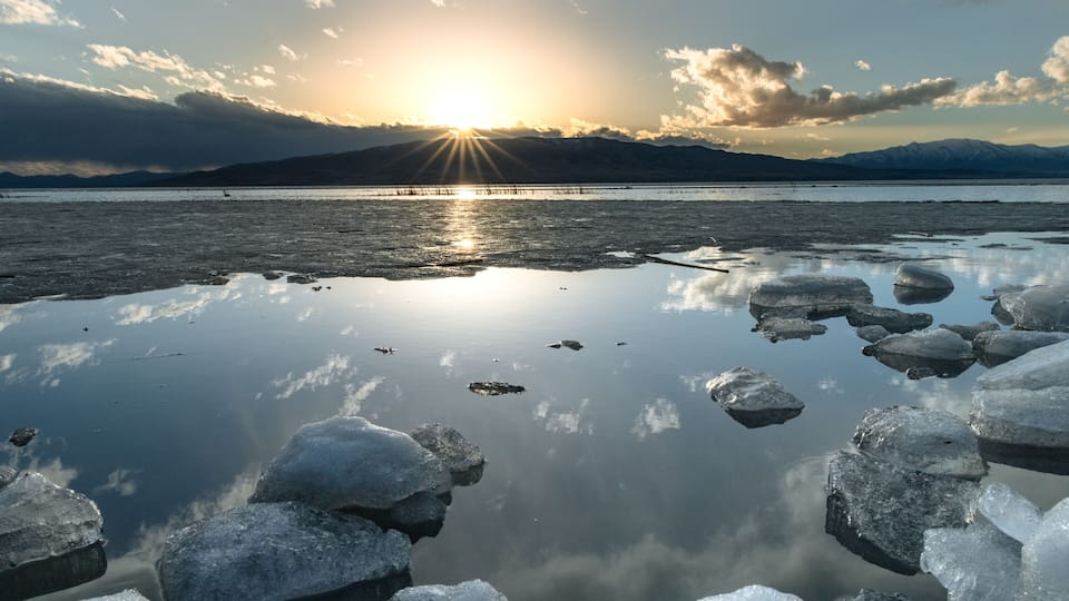 Ice stacks in horizontal image at Vineyard Beach on Utah Lake in Utah at sunset with sun star in February 2025.