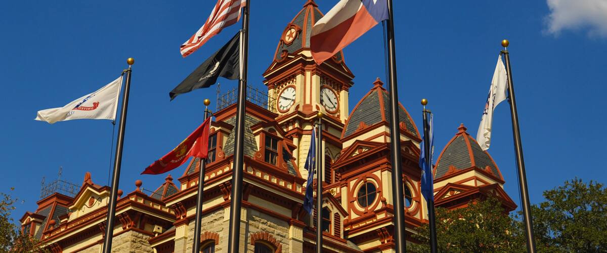 A historic building with multiple flags, including the American flag, and a clock tower.
