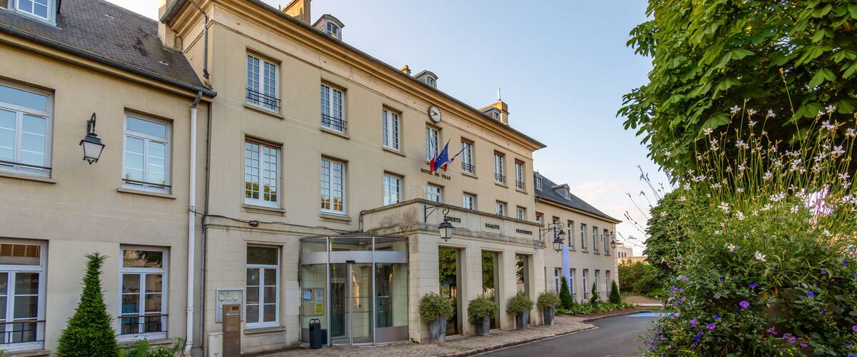 A historic building with a clock, a flag, and a well-maintained garden.