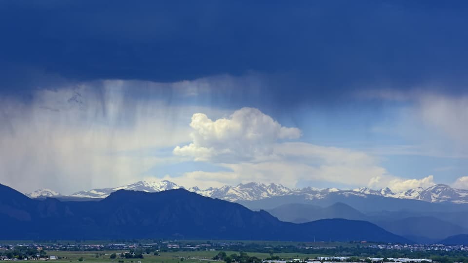 A mountainous landscape with snow-capped peaks, a town in the foreground, and a dramatic sky with clouds.