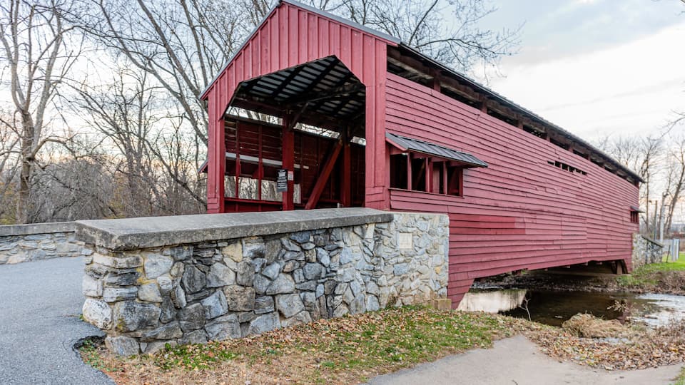 A red covered bridge with stone walls and a stone foundation.