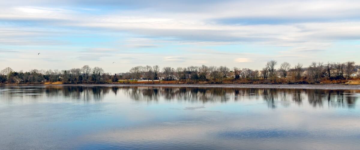 A calm lake reflecting the sky and trees, with houses along the shore.