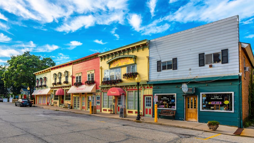 A row of colorful buildings with awnings, a street, and a clear blue sky with clouds.