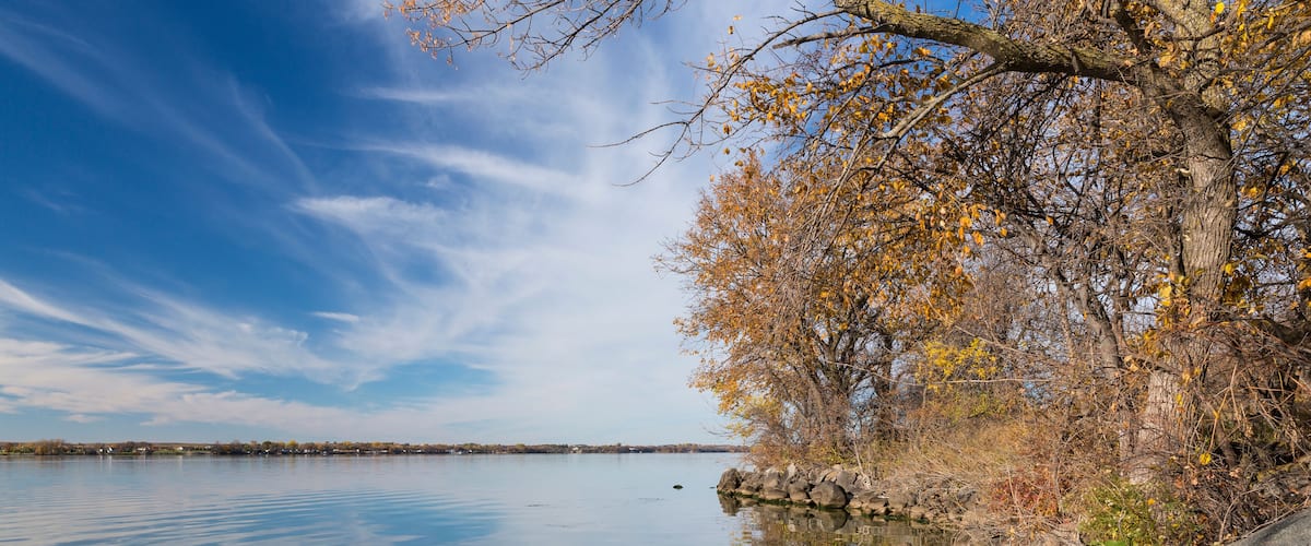 A calm lake with clear reflections, surrounded by autumn-colored trees and rocky shores.