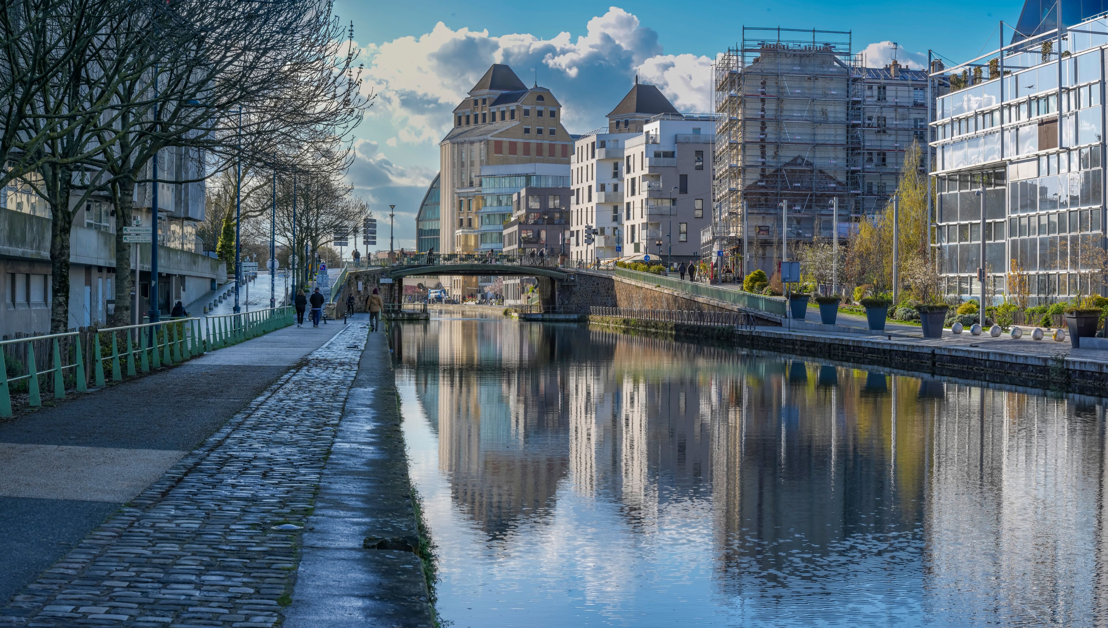 Paris, France - 03 14 2026: Ourcq Canal. Panoramic view of Les Grands Moulins of Pantin, City Hall Footbridge and buildings reflecting on the water