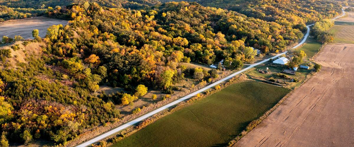 An aerial view of a winding road through a forested area with fields on either side.