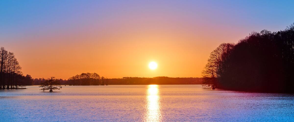A sunset over a calm lake with trees silhouetted against the sky.