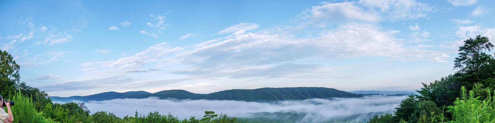 panorama of senior female photographer making pictures of fog in the valley below a scenic overlook along the skyway motorway in the talladega national forest, alabama, usa