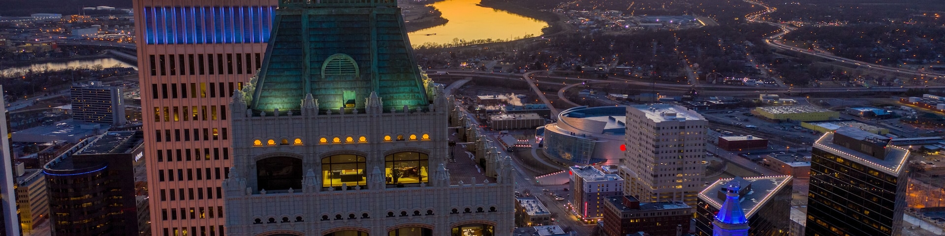 A cityscape with a prominent building featuring a green-lit tower and a river in the background.